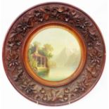 A Swiss Black Forest carved wood wall plaque with decorative border and central painted mountain