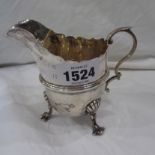 A silver cream jug with shaped rim and cast scroll handle, set on shell topped paw pattern feet -