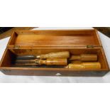 A lift-top wooden box containing four assorted chisels