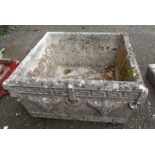 A square concrete garden planter with grapevine decoration