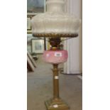A Victorian oil lamp with brass Corinthian column stand and opaque pink glass reservoir with chimney