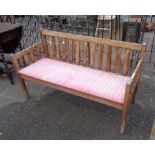 A two seater wooden slatted garden bench with upholstered drop-in seat