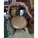 An old mahogany framed bow back swivel elbow chair with damaged rattan seat panel, set on quadrule