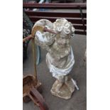 An old concrete garden statue depicting a cherub playing a tamborine