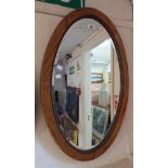 An oak framed bevelled oval wall mirror with beaded border