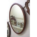 An antique mahogany and checkerboard strung bevelled oval wall mirror