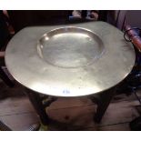 A 51cm diameter brass dished tray topped table with incised coat-of-arms decoration, set on a