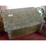 An old wooden embossed brass clad coal box of lift-top hutch form, the lid decorated with a scene of
