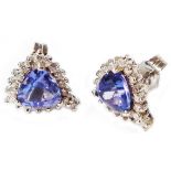 A pair of white metal earrings, each set with a central triangular tanzanite within a diamond