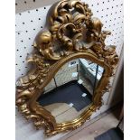A gilt plaster framed ornate wall mirror in the Rococo style with shaped plate