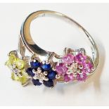 A marked 10K white metal triple flowerhead pattern crossover ring, set with pink, blue and yellow