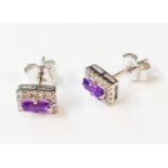 A pair of marked 585 white metal stud earrings, each set with central oblong amethyst within a