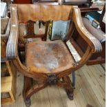 An old carved oak framed Italian X-frame elbow chair with slung studded leather back and seat