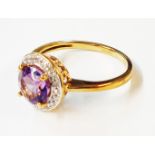A 375 (9ct.) gold ring, set with a central round cut amethyst within a diamond encrusted border -