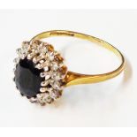 A 375 (9ct.) gold ring, set with a central dark oval sapphire within a diamond chip border - size