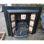 A 97cm Victorian black painted cast iron fire grate with repeat floral pattern to edges, ceramic