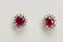 A PAIR OF 9CT WHITE GOLD CLUSTER EARRINGS, of an oval form, centring on an oval cut ruby, within a