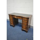 A REPRODUCTION MAHOGANY SERPENTINE KNEE HOLE DESK, with green leather and tooled inlay, and nine