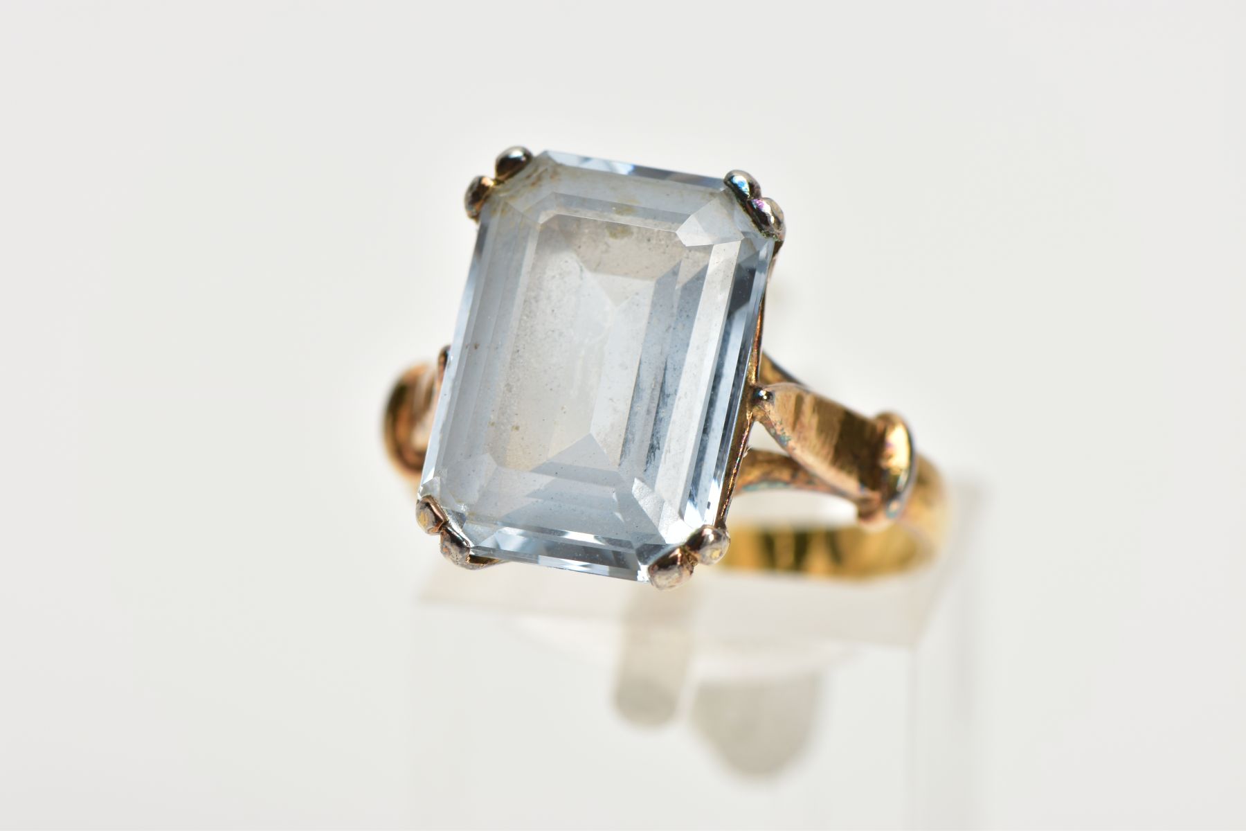 A YELLOW METAL AQUAMARINE DRESS RING, designed with a four claw set, rectangular cut aquamarine,