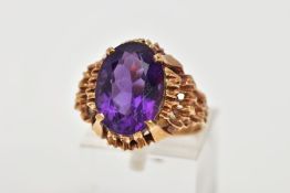 A YELLOW METAL AMETHYST DRESS RING, designed with a claw set oval cut amethyst, to an openwork
