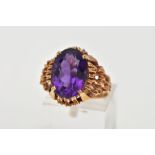 A YELLOW METAL AMETHYST DRESS RING, designed with a claw set oval cut amethyst, to an openwork