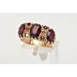 A 9CT GOLD GARNET RING, three oval cut garnets claw set in a yellow gold band with small circular