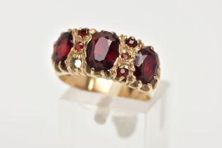 A 9CT GOLD GARNET RING, three oval cut garnets claw set in a yellow gold band with small circular