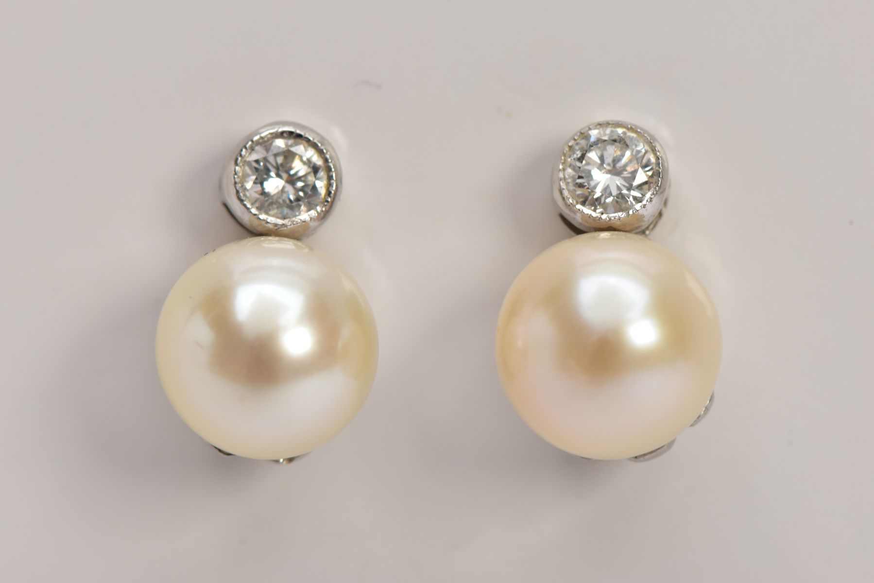 A PAIR OF WHITE METAL DIAMOND AND CULTURED PEARL EARRINGS, each designed with a single cultured