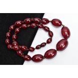 A CHERRY AMBER BAKELITE BEAD NECKLACE, graduated oval beads individually knotted onto a brown