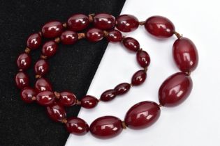 A CHERRY AMBER BAKELITE BEAD NECKLACE, graduated oval beads individually knotted onto a brown