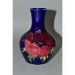 A MOORCROFT POTTERY BOTTLE SHAPED VASE DECORATED WITH RED/MAUVE ANEMONE ON A BLUE GROUND,