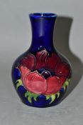 A MOORCROFT POTTERY BOTTLE SHAPED VASE DECORATED WITH RED/MAUVE ANEMONE ON A BLUE GROUND,