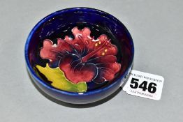 A SMALL MOORCROFT POTTERY FOOTED BOWL, with tubelined red/blue Hibiscus pattern on a dark blue