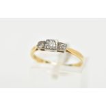 A YELLOW METAL THREE STONE DIAMOND RING, centring on a round brilliant cut diamond within a square