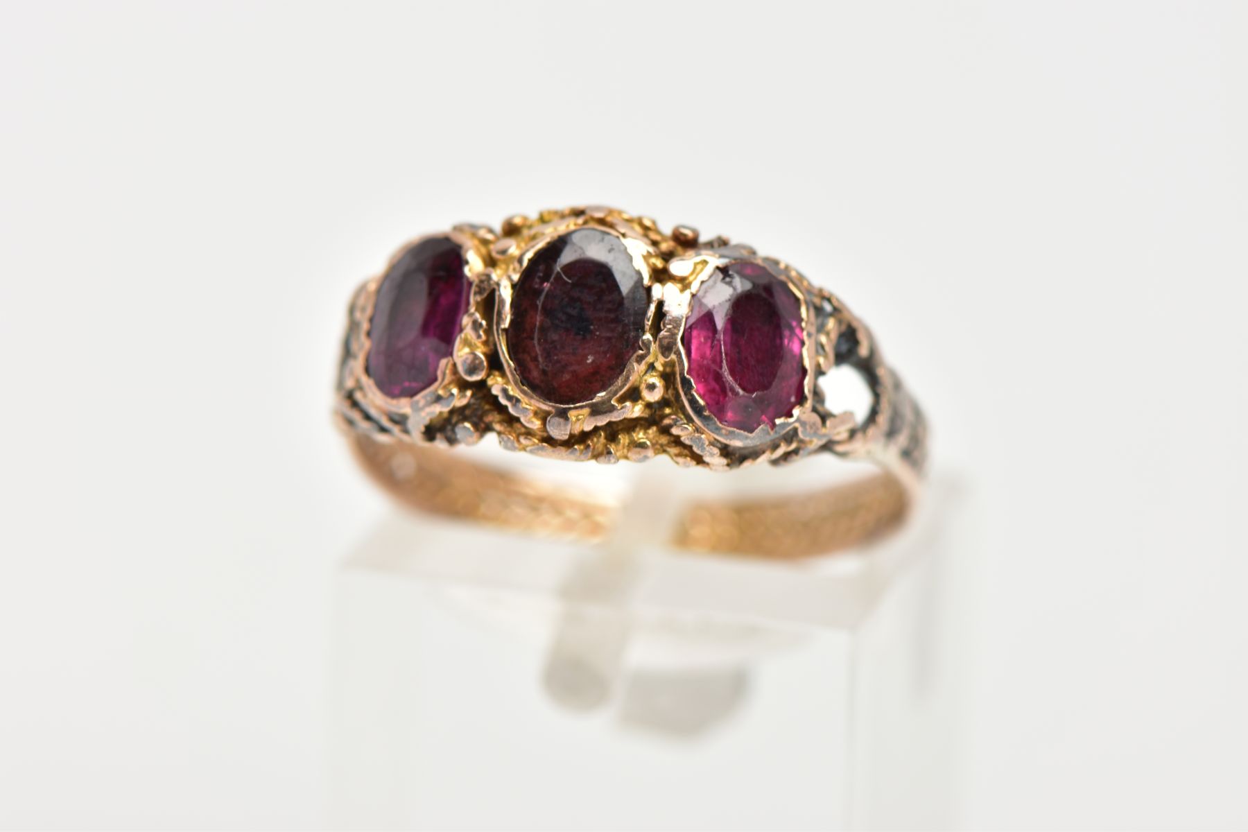 A THREE STONE GARNET RING, three oval cut garnets set within a rope twist surround leading on to the