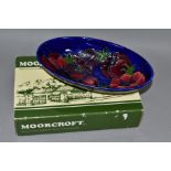 A BOXED MOORCROFT POTTERY OVAL BOWL DECORATED WITH RED / MAUVE ANEMONE ON A BLUE GROUND, painted and