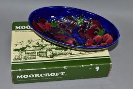 A BOXED MOORCROFT POTTERY OVAL BOWL DECORATED WITH RED / MAUVE ANEMONE ON A BLUE GROUND, painted and