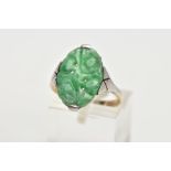 A JADEITE RING, an oval carved jadeite panel set in a white metal with tapered shoulders leading