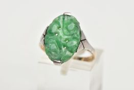 A JADEITE RING, an oval carved jadeite panel set in a white metal with tapered shoulders leading