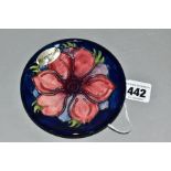 A MOORCROFT POTTERY CIRCULAR PIN DISH DECORATED WITH A RED/MAUVE ANEMONE ON A BLUE GROUND, with oval