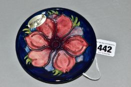 A MOORCROFT POTTERY CIRCULAR PIN DISH DECORATED WITH A RED/MAUVE ANEMONE ON A BLUE GROUND, with oval