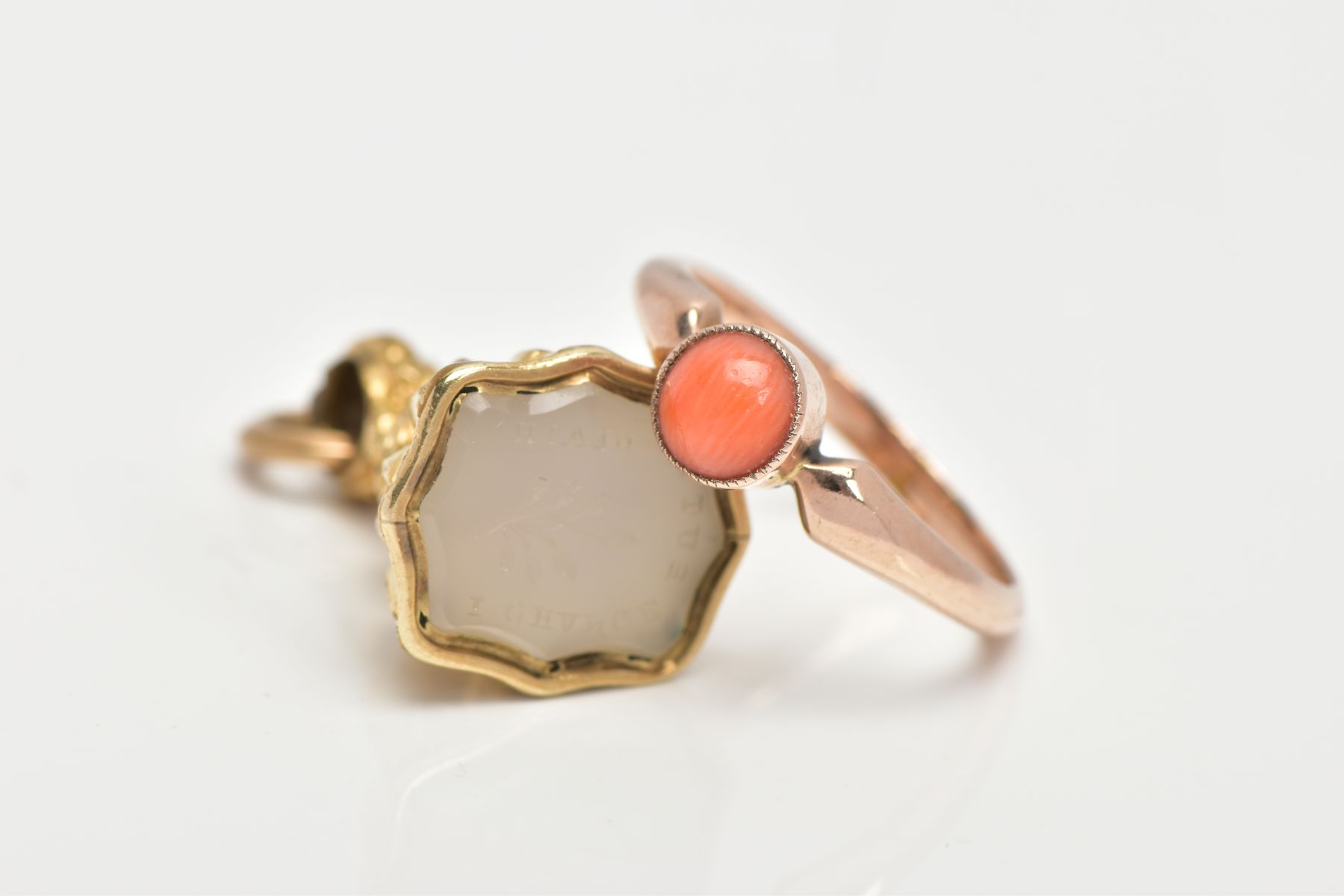 A CORAL RING AND INTAGLIO FOB, a round cabochon coral stone milgrain set in a rose metal mount,