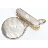 A SILVER VANITY MIRROR AND CLOTHES BRUSH, the mirror of a round form, engine turned design and