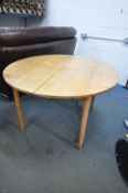 A MID CENTURY TEAK CIRCULAR EXTENDING DINING TABLE, with a single fold out leaf, extended length