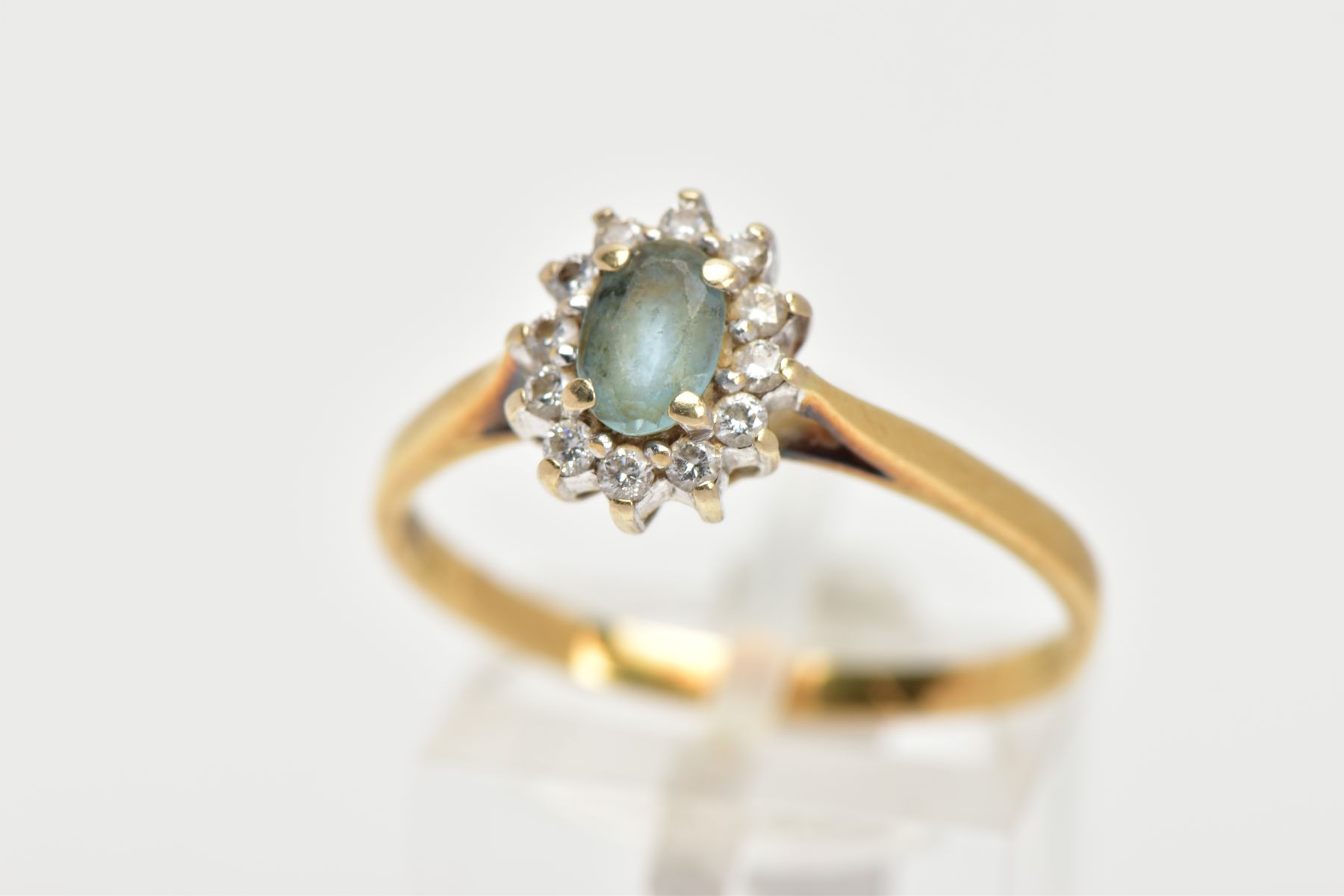 AN 18CT GOLD GEM SET CLUSTER RING, of an oval form, centring on an oval cut aquamarine, within a