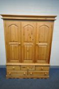 A PINE DOUBLE DOOR WARDROBE, fitted central panel, above a base with an arrangement of five drawers,