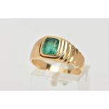 A YELLOW METAL EMERALD SIGNET RING, centring on an emerald cut emerald, bezel set, textured design