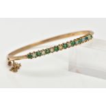 A 9CT GOLD EMERALD AND OPAL BANGLE, hinged bangle, designed with a row of circular cut emeralds
