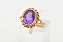 A 9CT GOLD AMETHYST DRESS RING, an oval cut amethyst set in a yellow gold bezel setting and a rope