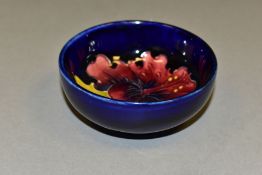 A SMALL MOORCROFT POTTERY FOOTED BOWL, with tubelined red/blue Hibiscus pattern on a dark blue